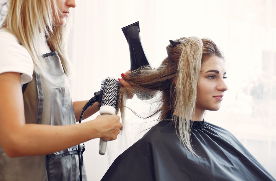 Cabeleireiro corta e penteia o cabelo com secador para senhora loira