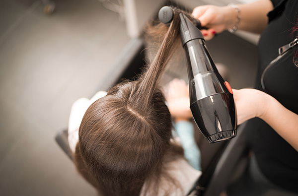 Cabeleireiro seca o cabelo com uma mulher de secador de cabelo no