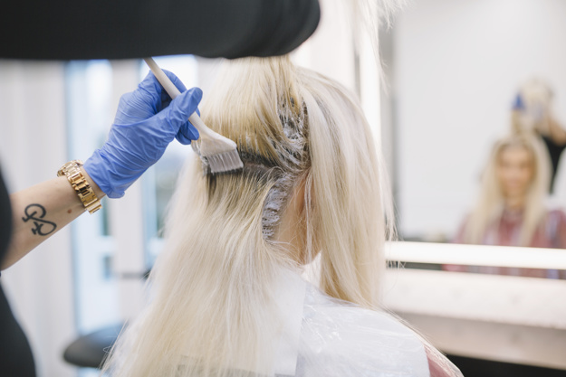 cabelereiro aplicando tinta na raiz de cabelo da cliente loira