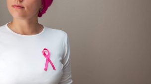 mulher de lenço nos cabelos com símbolo do outubro rosa em sua camisa