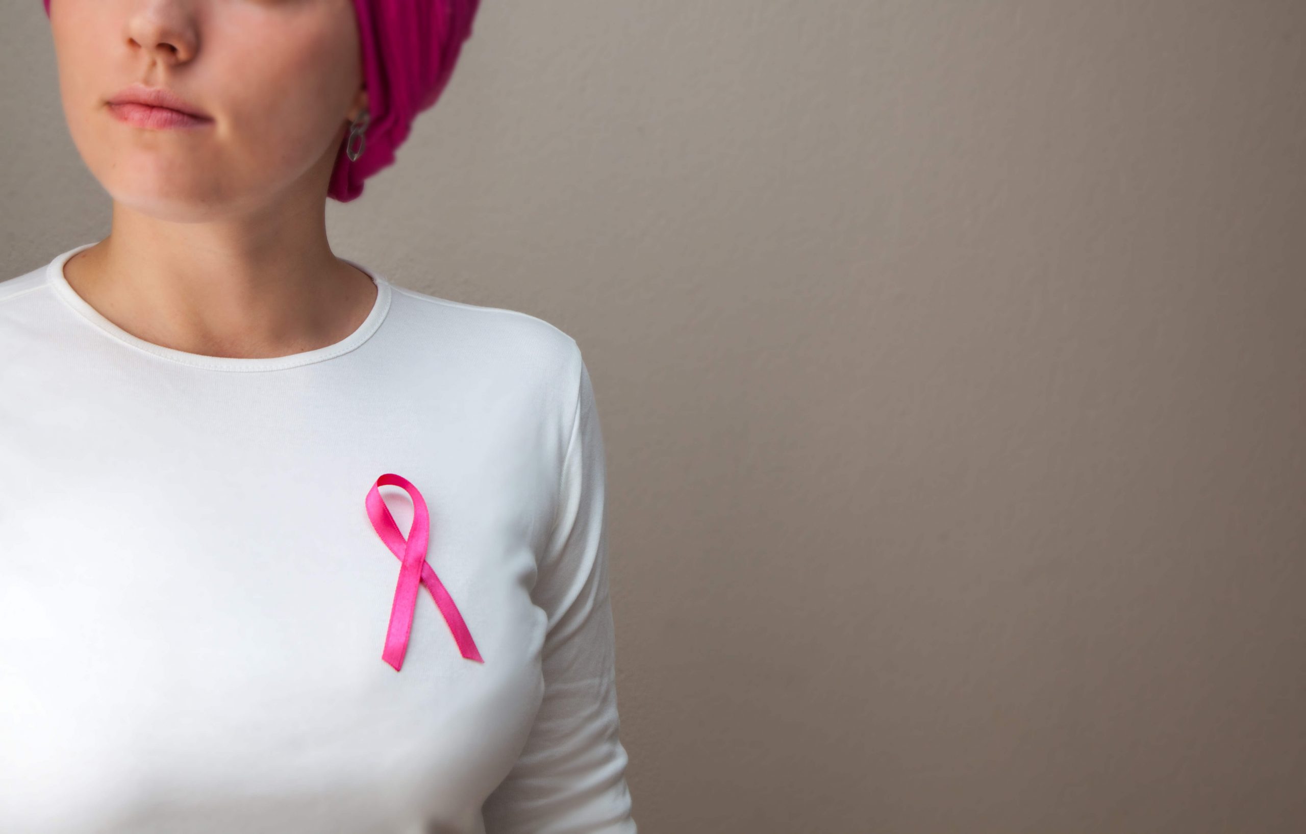 mulher de lenço nos cabelos com símbolo do outubro rosa em sua camisa